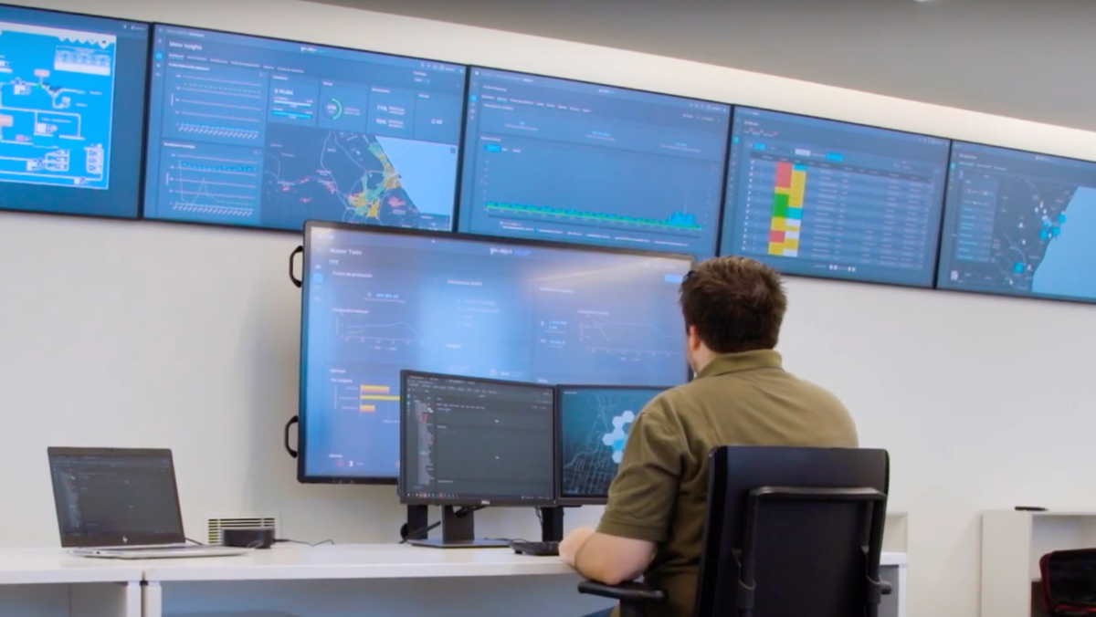 Operator monitors multiple digital dashboards showing smart water network data in a modern control room.
