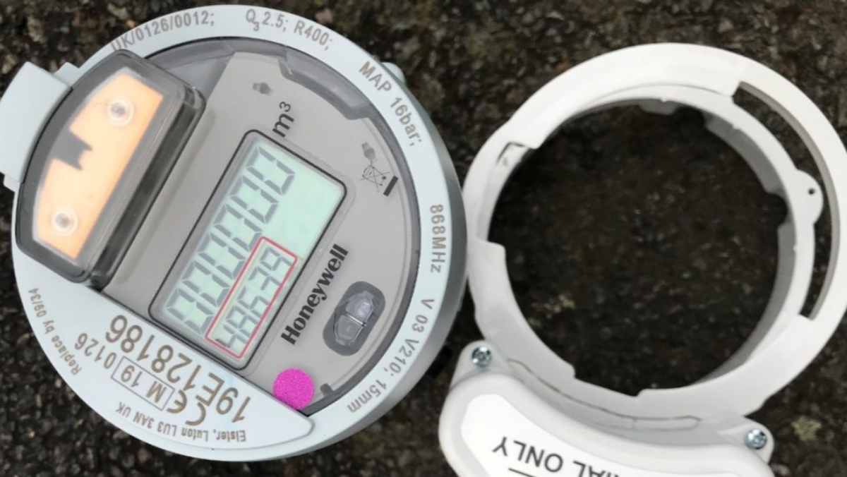 Close-up of digital smart water meter with display and casing on ground.
